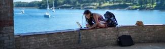 student sitting with laptop near ocean